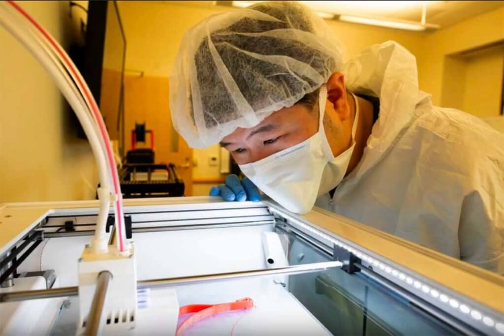 man in scrubs watching a 3D printer at work