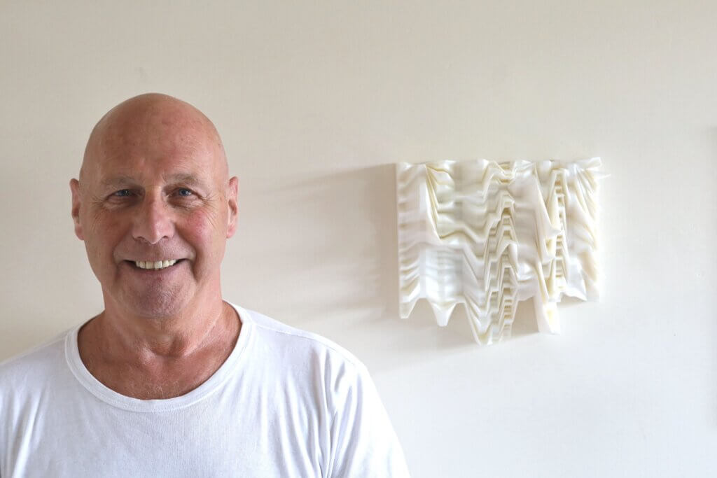 Mick O' Kelly, PhD, MFA, BFA, pictured next to blank wall with 3D print of his REM sleep waves.