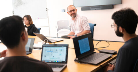 Five people holding a meeting at a conference room table with laptops in front of them.