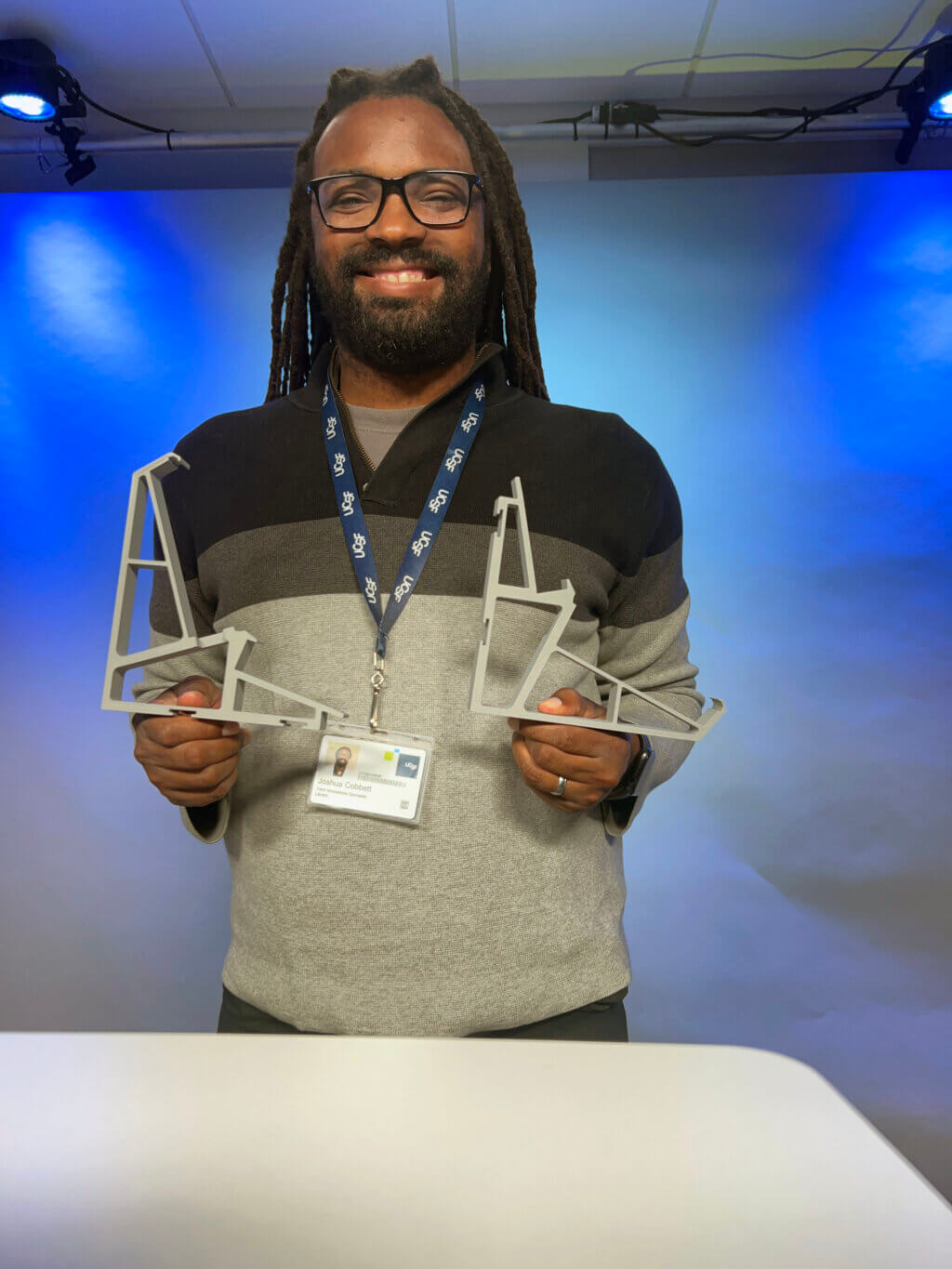 Joshua holding custom 3D printed mounts in UCSF Library digital media suite.