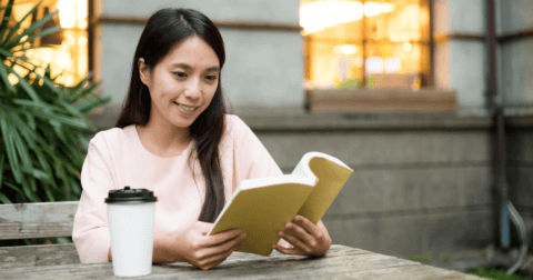 A woman reading a book while seated outdoors.